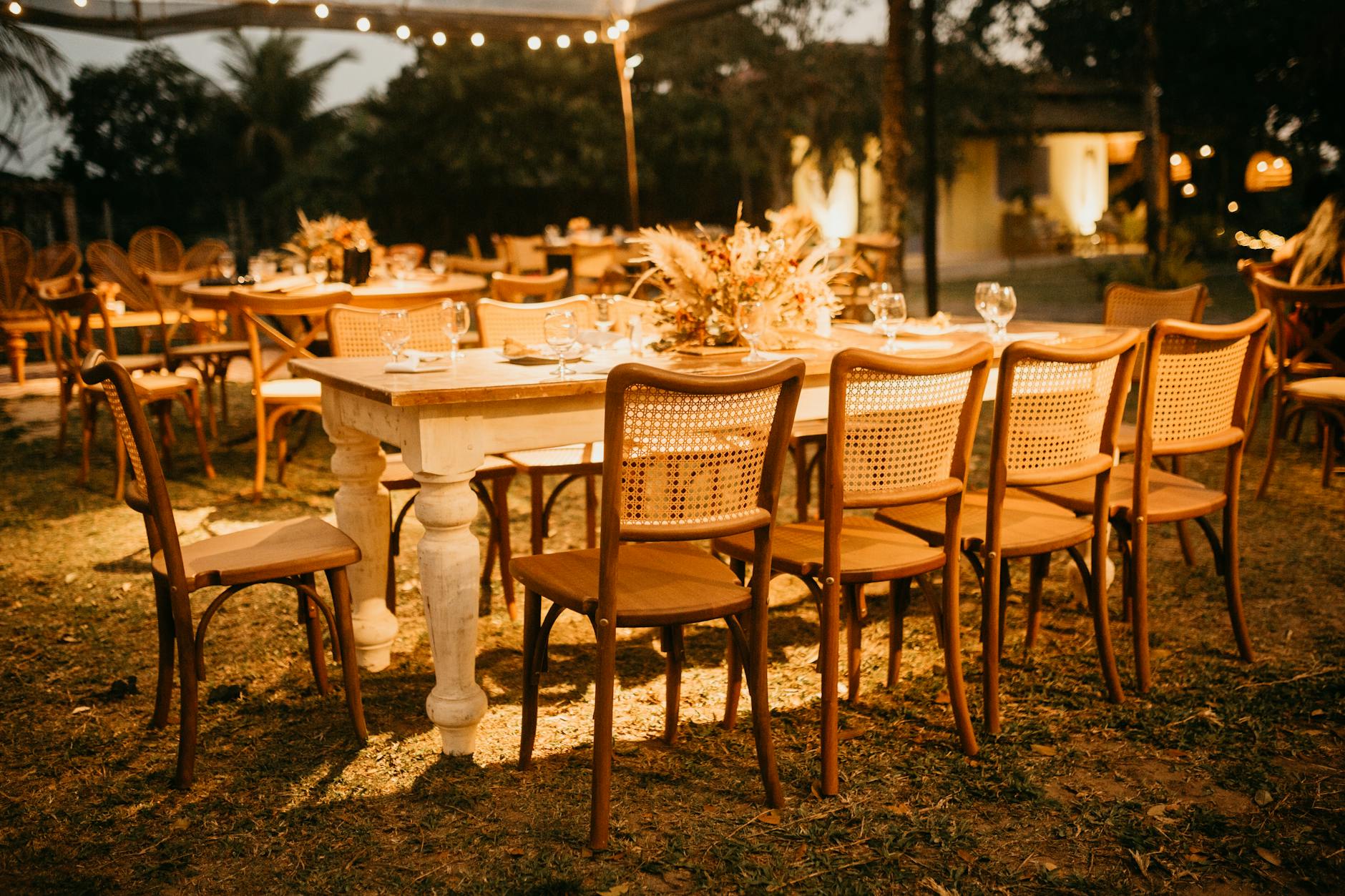 intimate outdoor wedding dinner with a long table of about 30 guests under string lights and greenery, warm sunset lighting