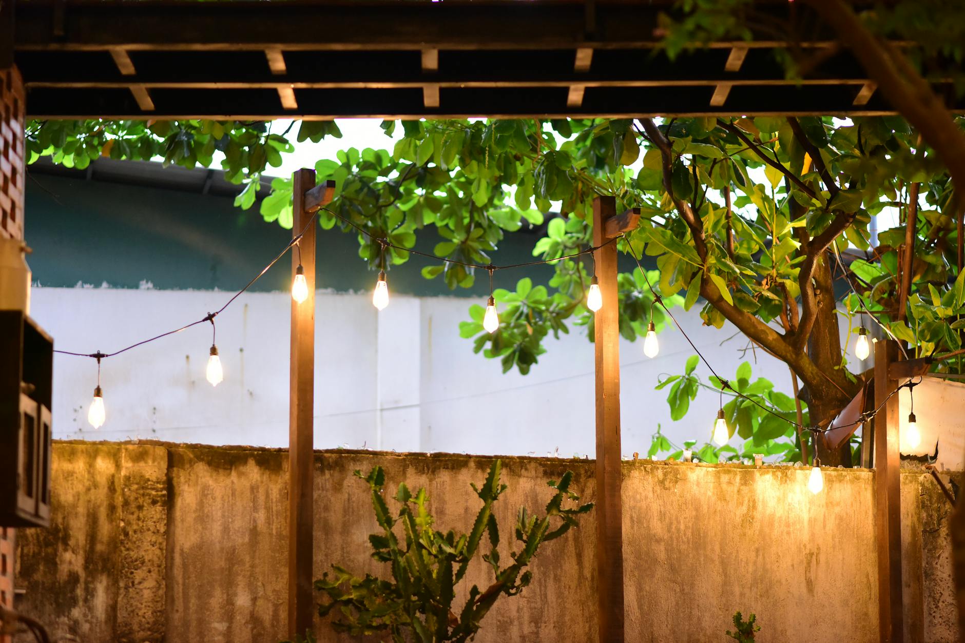 Budget-Friendly Patio Makeover Ideas for Summer 2 modern patio with a beige shade sail, potted greenery, and warm string lights at golden hour