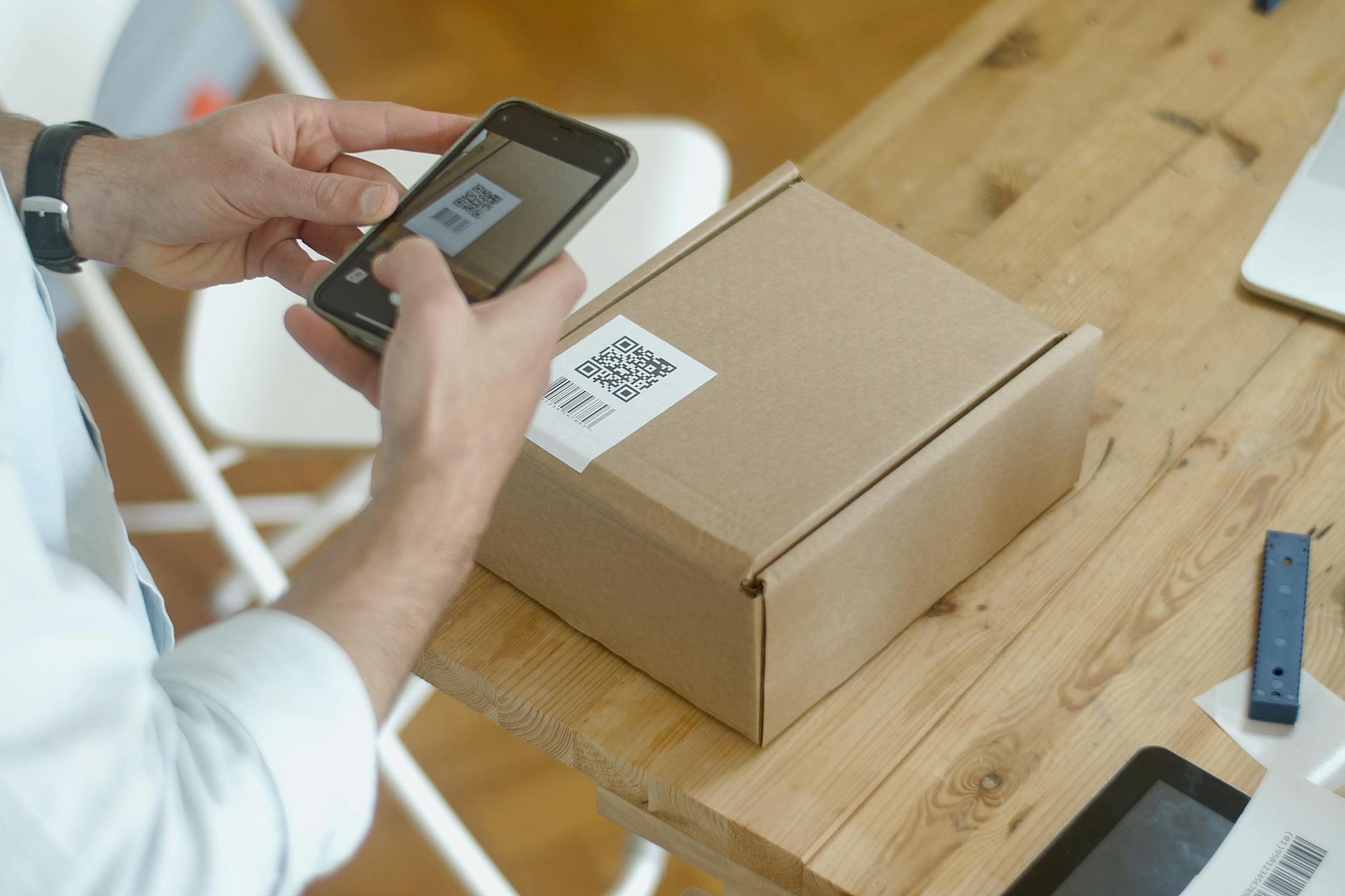 person holding a small parcel and a QR code on their phone at a staffed drop-off counter with shipping scales and signage